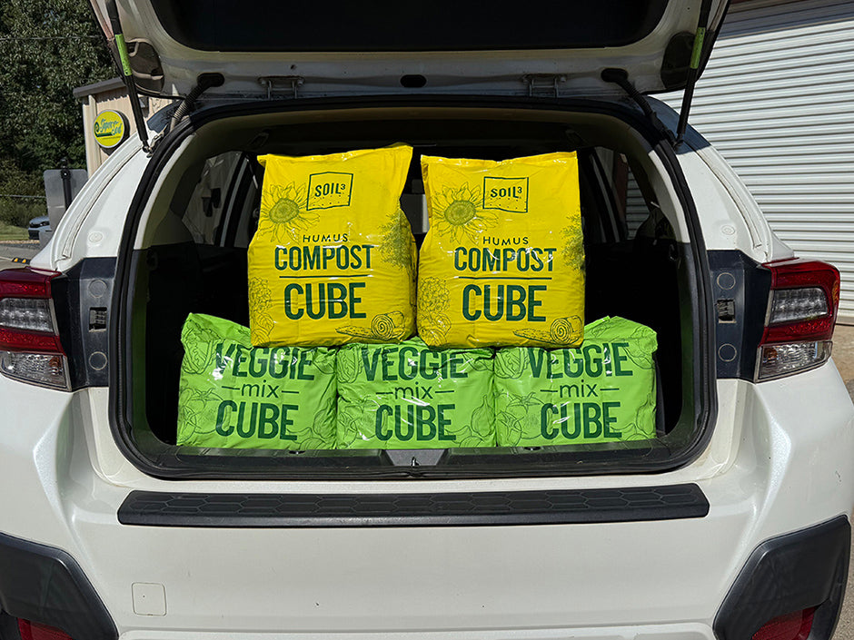 Three bags labeled 'Compost Cube' and 'Veggie Mix Cube' in the trunk of a white car.