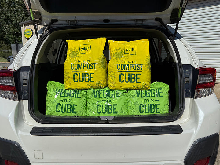 Three bags labeled 'Compost Cube' and 'Veggie Mix Cube' in the trunk of a white car.